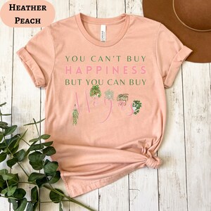May include: A peach colored t-shirt with the text "You can't buy happiness but you can buy Hoyas" with a graphic of potted plants.