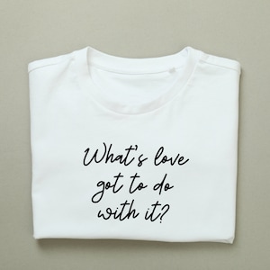 Op de afbeelding: Wit T-shirt met de tekst "What's love got to do with it?" in zwart gedrukt.