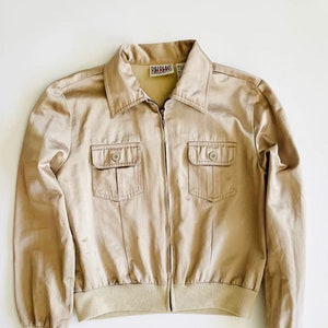 May include: A beige zip-up jacket with a collared neckline and two flap pockets. The jacket has a Bill Blass label on the front.