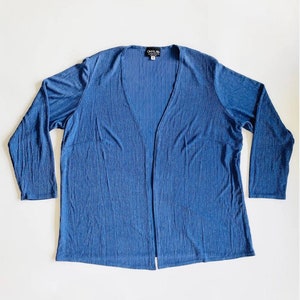 May include: A blue, long-sleeved cardigan with a V-neck and a sparkly texture. The cardigan is open in the front and has a small tag that says "Crystal" on it.