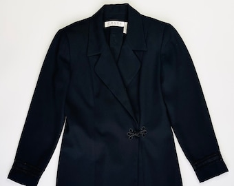 May include: A black long-sleeved wrap dress with a collar and a decorative knot closure. The dress has a label that reads "CHAUS".