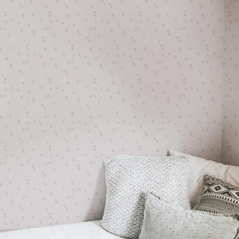 May include: A light pink wall with a subtle pattern of small gray leaves. A white bed with a gray knitted throw pillow and two white pillows is in the corner of the room.