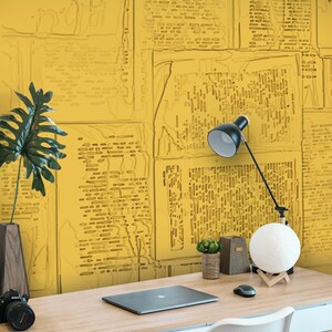 May include: A yellow desk with a laptop, a lamp, a moon lamp, and two small potted plants. The wall behind the desk is covered in a yellow wallpaper with a pattern of overlapping newspaper clippings.