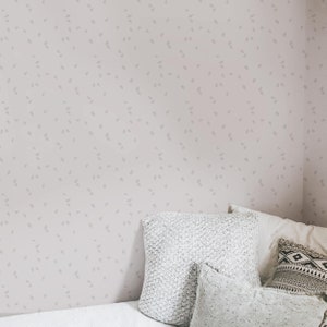 May include: A light pink wall with a subtle pattern of small gray leaves. A white bed with a gray knitted throw pillow and two white pillows is in the corner of the room.