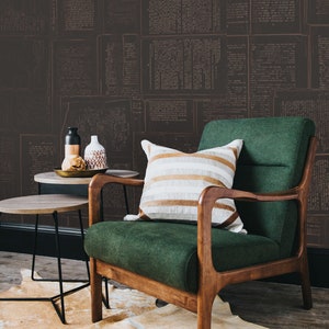May include: A green armchair with wooden legs and arms, a striped throw pillow, and two small side tables. The armchair is in front of a wall covered in a wallpaper with a pattern of old newspaper pages.