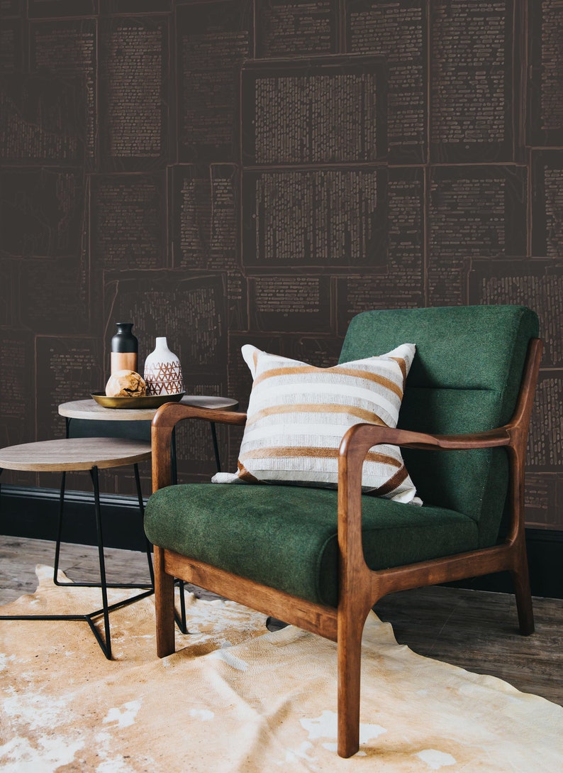 May include: A green armchair with wooden legs and arms, a striped throw pillow, and two small side tables. The armchair is in front of a wall covered in a wallpaper with a pattern of old newspaper pages.