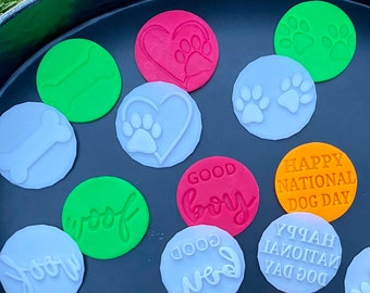 Pode incluir: Uma coleção de 17 cortadores de biscoitos redondos coloridos com designs temáticos de cães, incluindo pegadas, ossos, corações e frases como "Good Boy", "Woof" e "Happy National Dog Day".