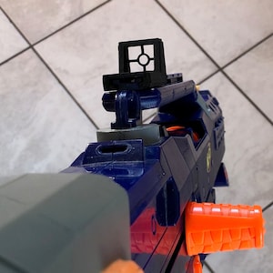 May include: A blue and orange toy blaster with a black scope sight. The blaster has a textured orange grip and a black barrel.