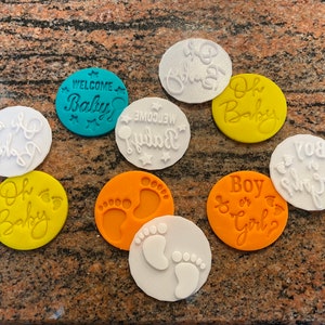 Pode incluir: Nove cortadores de biscoitos redondos com v&aacute;rios desenhos tem&aacute;ticos de beb&ecirc;. Os desenhos incluem "Bem-vindo beb&ecirc;", "Oh beb&ecirc;", "Menino ou menina?", "Voc&ecirc; &eacute; meu sol" e pegadas. Os cortadores s&atilde;o de v&aacute;rias cores, incluindo branco, amarelo, laranja e azul.