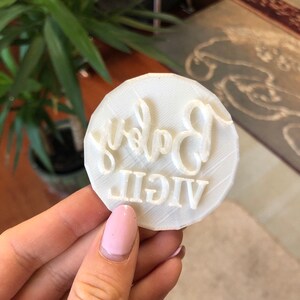 Pode incluir: Carimbo de biscoito de pl&aacute;stico branco com as palavras "VIGIL Baby" em relevo.