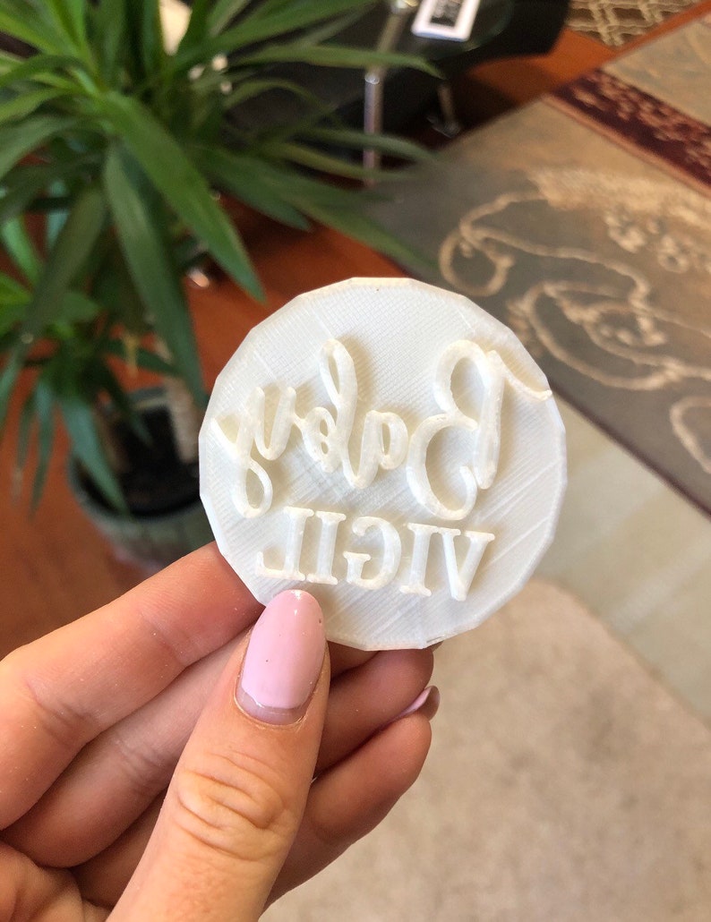 Pode incluir: Carimbo de biscoito de pl&aacute;stico branco com as palavras "VIGIL Baby" em relevo.