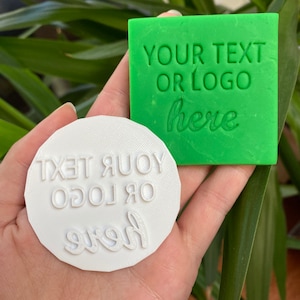 May include: Two white and green rubber stamps with the text "YOUR TEXT OR LOGO here" on them. The stamps are used for crafting and creating personalized items.