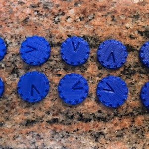 May include: Ten blue plastic tokens with a raised 'V' on each. The tokens are circular and have a textured edge.