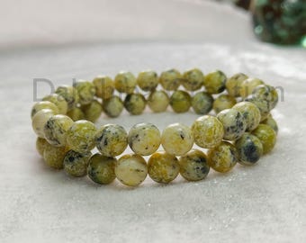 May include: Two beaded bracelets. Each bracelet is made of round, light green and yellow beads with dark spots. The bracelets are stacked on top of each other. The beads have a polished finish.