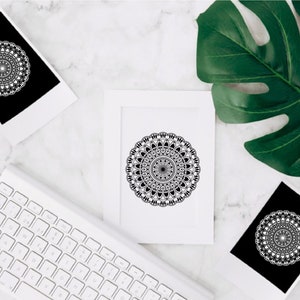 Op de afbeelding: Drie zwart-witte mandala-ontwerpen gedrukt op wit karton. De mandala's zijn ingewikkeld en gedetailleerd, met een cirkelvormig patroon van geometrische vormen. De ontwerpen zijn ingelijst en worden weergegeven op een wit marmeren oppervlak.