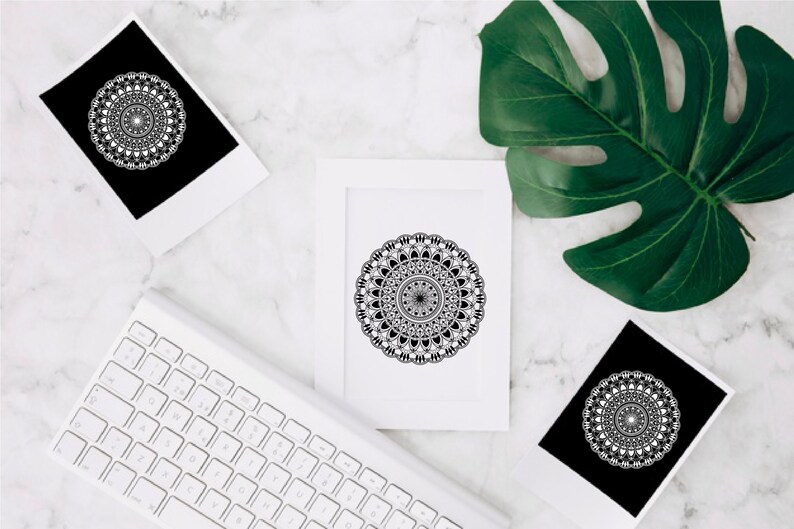 Op de afbeelding: Drie zwart-witte mandala-ontwerpen gedrukt op wit karton. De mandala's zijn ingewikkeld en gedetailleerd, met een cirkelvormig patroon van geometrische vormen. De ontwerpen zijn ingelijst en worden weergegeven op een wit marmeren oppervlak.