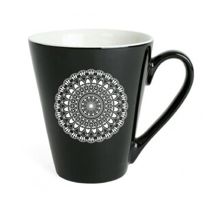 Op de afbeelding: Zwarte keramische mok met een wit mandala-ontwerp. De mok heeft een brede basis en een handvat.