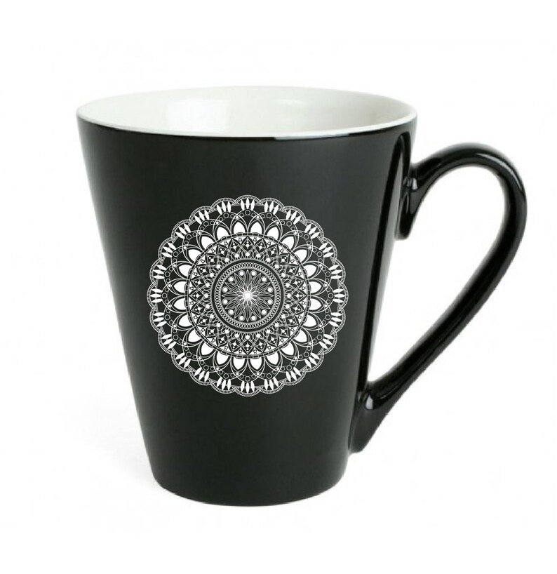 Op de afbeelding: Zwarte keramische mok met een wit mandala-ontwerp. De mok heeft een brede basis en een handvat.