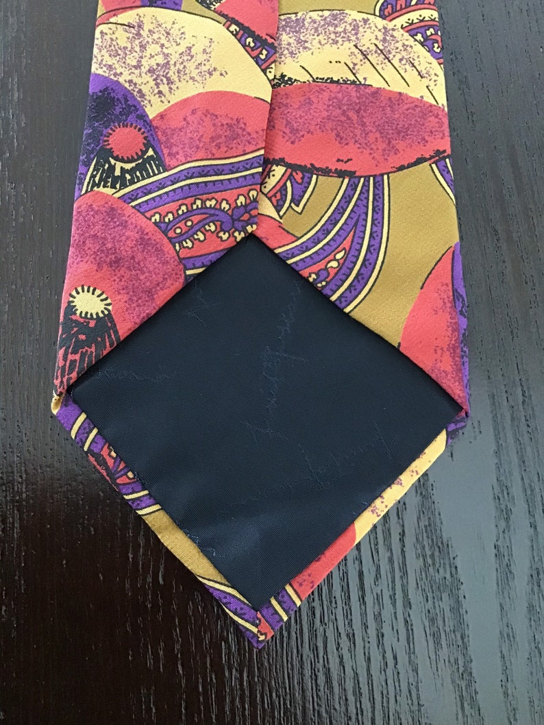May include: A silk tie with a colorful paisley pattern in shades of red, yellow, purple, and brown. The tie has a black lining.