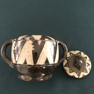 May include: A black and white ceramic pot with two handles and a matching lid. The pot has a geometric pattern.