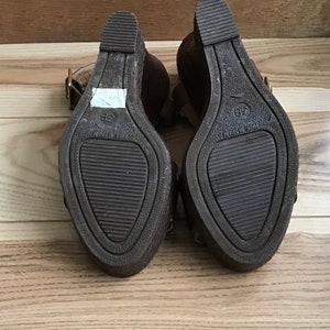 May include: A pair of brown wedge sandals with a buckle closure. The sandals have a textured sole and are marked with the size 38.