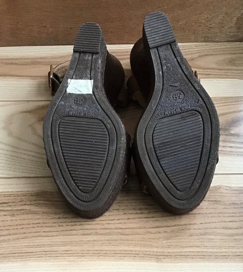May include: A pair of brown wedge sandals with a buckle closure. The sandals have a textured sole and are marked with the size 38.