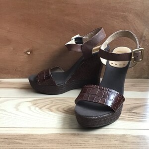 May include: A pair of brown wedge sandals with a crocodile-embossed leather strap and a woven platform.
