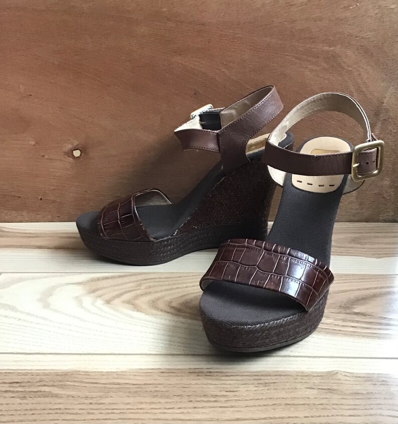 May include: A pair of brown wedge sandals with a crocodile-embossed leather strap and a woven platform.