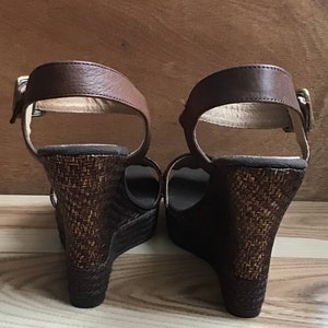 May include: A pair of brown wedge sandals with a woven platform and ankle straps.