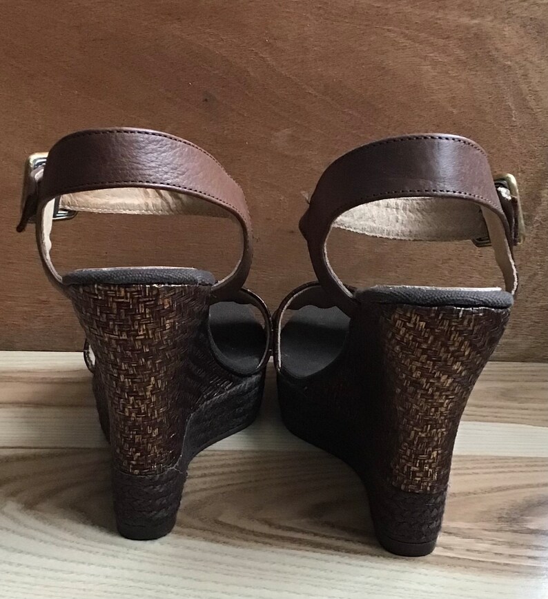 May include: A pair of brown wedge sandals with a woven platform and ankle straps.