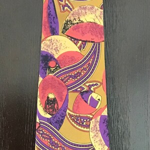 May include: A silk tie with a paisley pattern in shades of purple, pink, and yellow on a gold background.