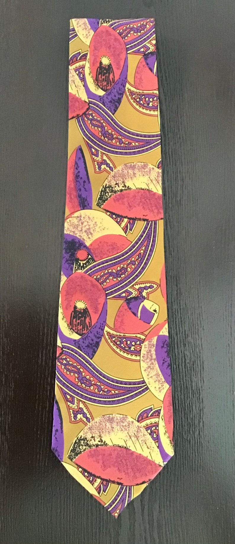May include: A silk tie with a paisley pattern in shades of purple, pink, and yellow on a gold background.