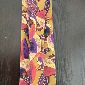 May include: A silk tie with a colorful abstract pattern featuring shades of purple, red, yellow, and brown. The tie has a black label that reads "Made in Italy".