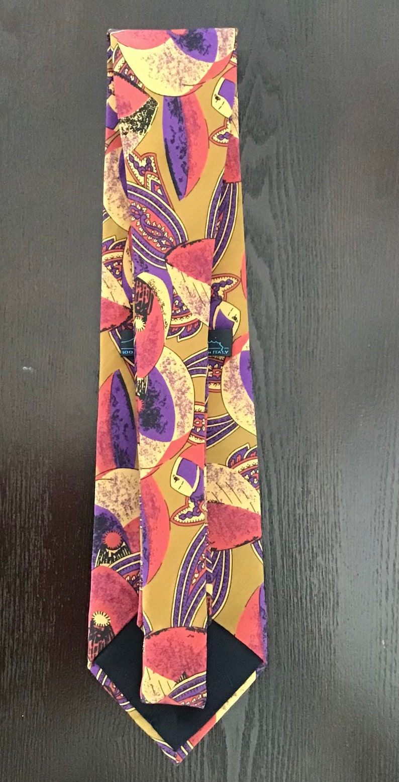 May include: A silk tie with a colorful abstract pattern featuring shades of purple, red, yellow, and brown. The tie has a black label that reads "Made in Italy".