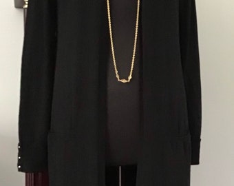 May include: A long black cardigan with a gold chain necklace. The cardigan has pockets on the sides and buttons on the cuffs.