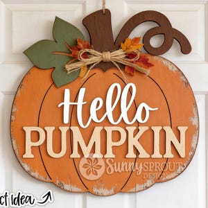 May include: A wooden pumpkin-shaped door sign painted orange with a distressed finish. It features the white text Hello and the beige text PUMPKIN. The top includes a brown stem, a green leaf, a jute twine bow, and artificial autumn leaves.