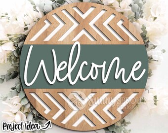 May include: A round wooden sign with a geometric pattern of white and brown arrows. The sign has a green band across the middle with the word "Welcome" written in white cursive.
