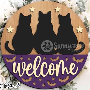 May include: A round wooden sign with a purple background and a welcome message. Three black cats are sitting on the top half of the sign, with stars and bats on the bottom half.