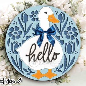 May include: A round, light blue wooden sign featuring a white duck with an orange beak and feet, and a blue bow. The word "hello" is written in cursive. The sign is surrounded by a floral design. The text "Project Idea" is in the bottom left corner.