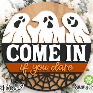 May include: A round wooden sign with three white ghosts and the text "COME IN if you dare" in black and orange. The sign has a black spiderweb design at the bottom.