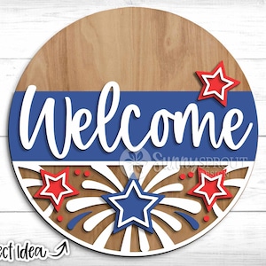 May include: A wooden round welcome sign with a blue and white striped band. The sign features the word "Welcome" in white lettering and a red, white, and blue firework design.