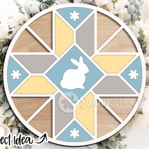 May include: A round wooden Easter-themed decoration with a geometric design. The design features a white bunny in a light blue square, surrounded by yellow, gray, and light blue shapes. The text "Project Idea" is visible at the bottom left.