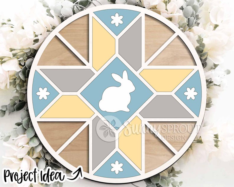 May include: A round wooden Easter-themed decoration with a geometric design. The design features a white bunny in a light blue square, surrounded by yellow, gray, and light blue shapes. The text "Project Idea" is visible at the bottom left.