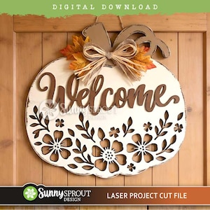 May include: A pumpkin-shaped wooden door sign with a distressed cream finish, featuring the word Welcome in brown script. The design includes laser-cut floral patterns, a burlap bow, and artificial orange and yellow autumn leaves at the top.