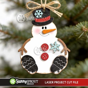 May include: A white wooden snowman ornament featuring a black top hat with a light blue snowflake, an orange carrot nose, two red buttons, a light blue snowflake accent, and black mittens with white zigzag patterns, suspended by a jute twine bow.