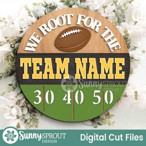 May include: A round wooden sign with a football and the text "WE ROOT FOR THE TEAM NAME". The sign has a green field with yard lines and the numbers 30, 40, and 50. The sign is surrounded by white flowers.