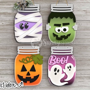 May include: Four Halloween-themed mason jar cutouts. The designs include a mummy, Frankenstein's monster, a jack-o'-lantern, and a jar with ghosts and the word "Boo!". Each jar has a lid and is ready to hang.