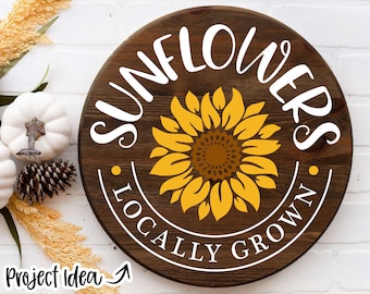 Może przedstawiać: Okrągły drewniany znak z napisem "Sunflowers Locally Grown" białymi literami. W środku znaku znajduje się żółty słonecznik z brązowym środkiem.