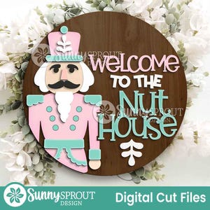 May include: A circular wooden sign featuring a pink and teal nutcracker design and the words "Welcome to the Nut House". The sign also includes the text "Sunny Sprout Design" and "Digital Cut Files".