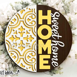 May include: Round wooden sign with a decorative design on the left and the words "HOME Sweet Home" in yellow and white. The left side features a yellow and white floral pattern. The sign is a home decor item.